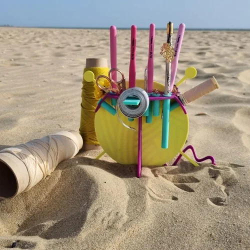 Vista trasera del organizador de labores OvilloAmor con agujas de colores en la playa